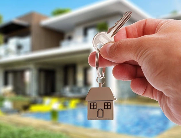 Hand holding house keys with a house-shaped keychain, new home buying concept.