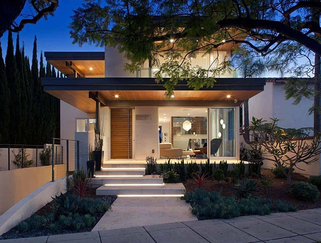 Modern two-story home with illuminated steps, landscaping, and large windows, ideal for property selling.