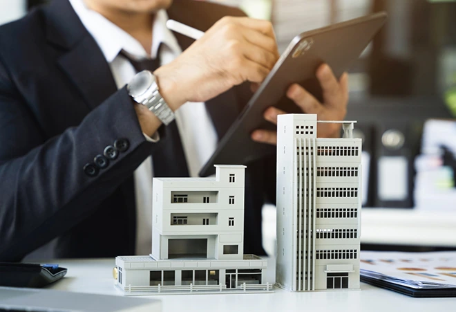 Commercial property models on a desk with a man reviewing documents for selling.