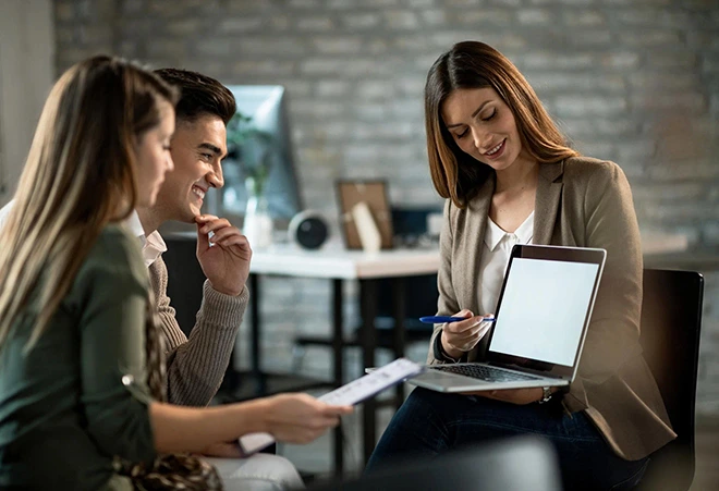 Investment property consultants showing a laptop to a couple in an office.