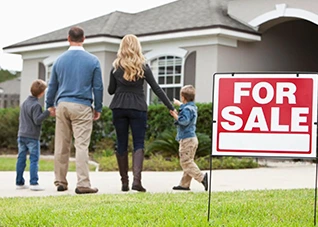 Family looking at a house with a "For Sale" sign. Selling a home.