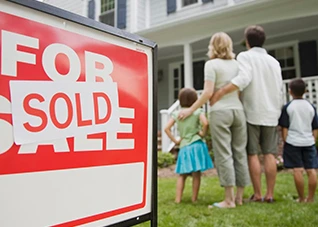 Family looks at house with "SOLD" sign. Selling a home, new homeowners.