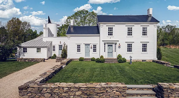 Charming white farmhouse with stone wall and manicured lawn, ideal for real estate.